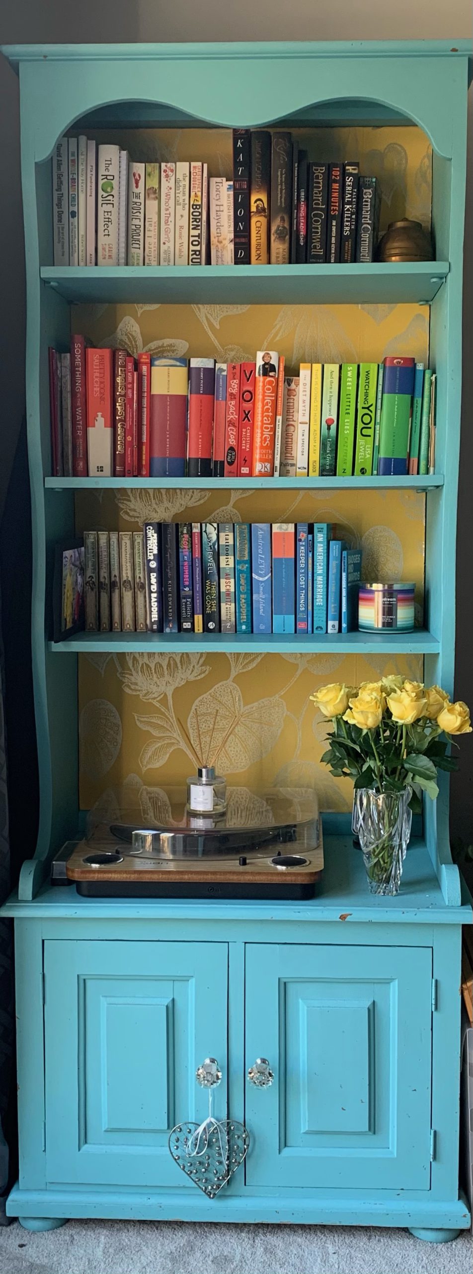 rainbow bookcase after being organised, books are in colour order on each shelf, with a vase of flowers near the bottom