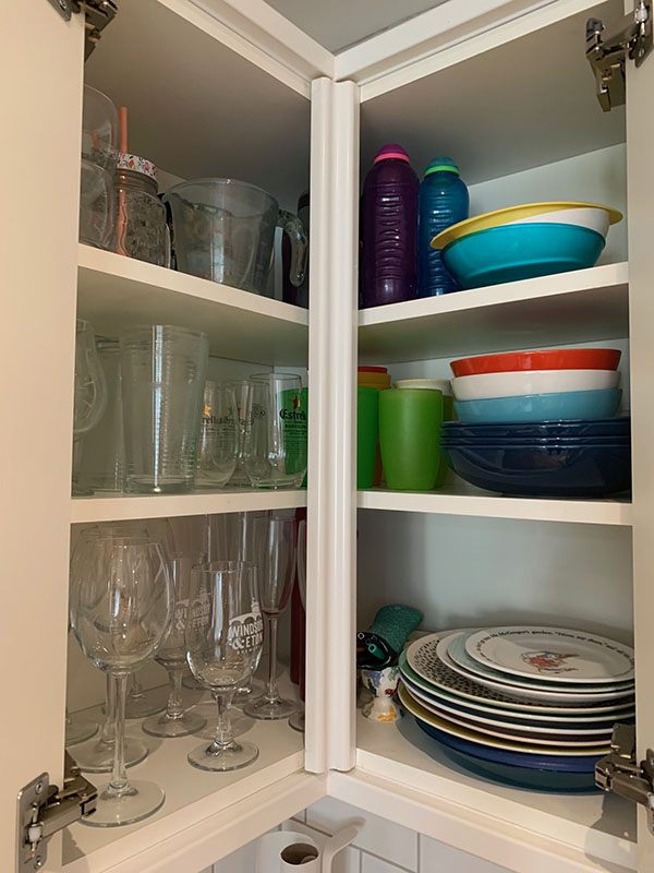 kitchen-11-800 A kitchen cupboard with organised glassware by type, plates and bowls, as well as drinking bottles