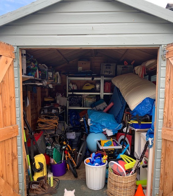 shed before Original loft area, everything is piled on the floor, with boxes and items haphazardly strewn around. There is no space to walk across the space to reach anything at the far wall